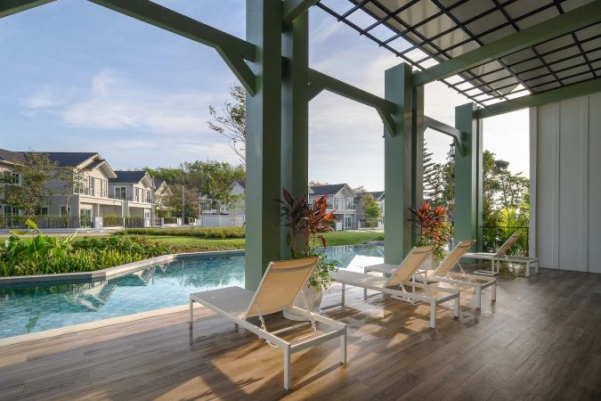A timber deck under the pergola with sun loungers at the pool edge, house facades across the water