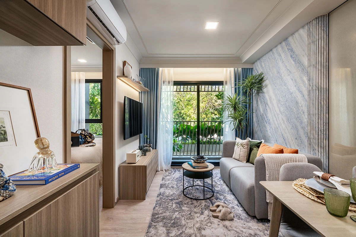 A unit's living room: a sofa and television along the wall, a stone-look panel and a balcony door onto greenery