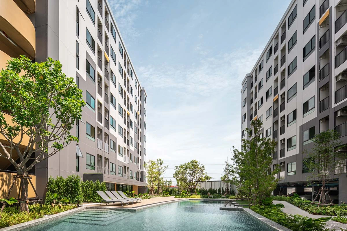 The courtyard at water level by day: the pool with its steps, three loungers at the edge, the eight-storey facades on both sides and a tree on the left