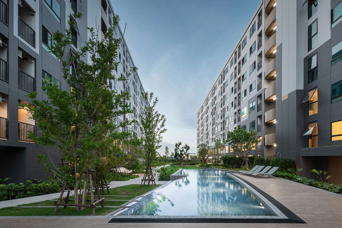 The same courtyard at dusk: lit water, a row of loungers on the right, glowing windows and balcony lights on the dark grey facade