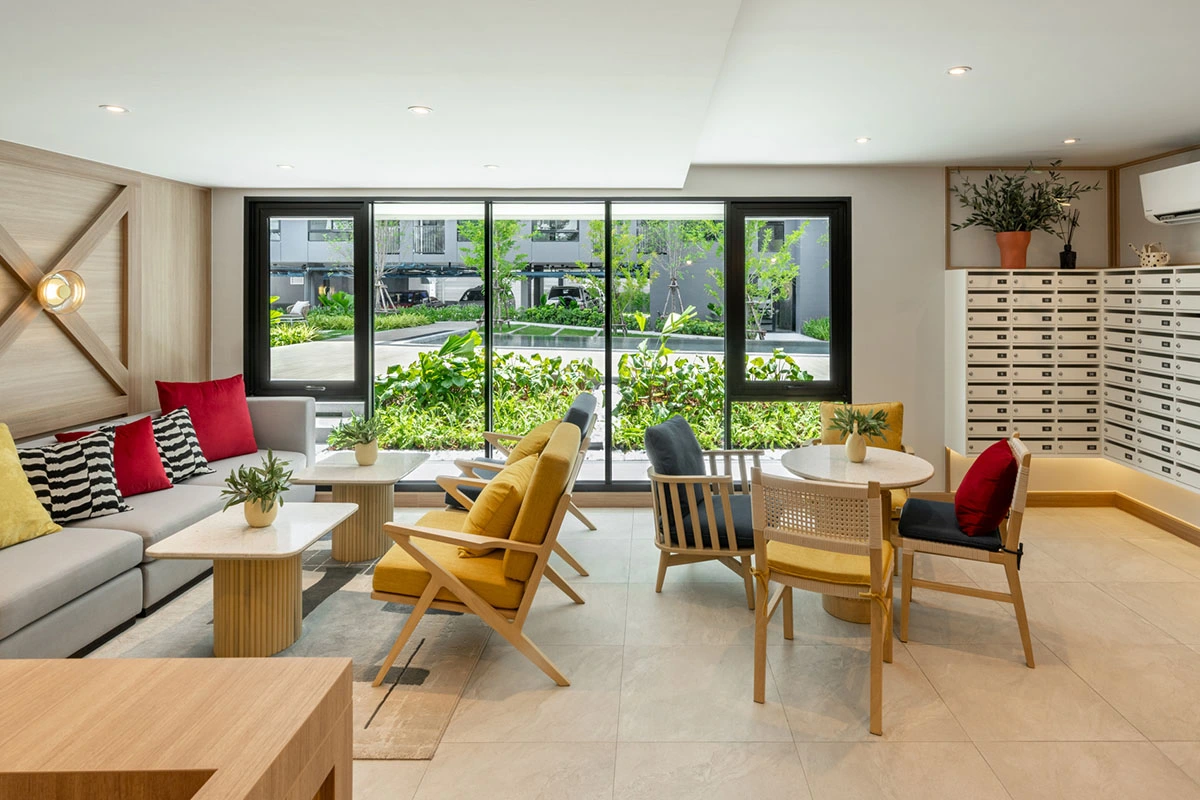 The lobby with its working area: a grey corner sofa, yellow and rattan chairs at a round table, windows onto the garden and a wall of letterboxes on the right