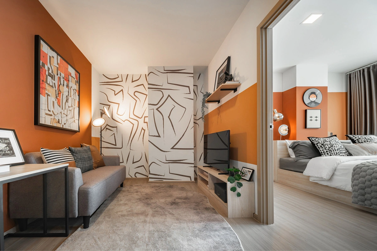 The living area of the same home: the sofa against the orange wall, the television on a low unit and, through the open doorway on the right, the bedroom with its bed