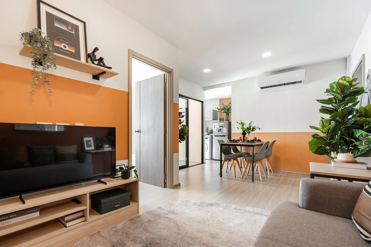 The view from the television: the hinged bedroom door, the sliding glass panel behind it and, at the far end, the kitchen with washing machine and fridge and the dining table for four