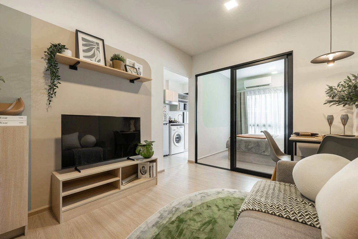 A living area: a television on a low unit, the bedroom visible behind the sliding glass panel and the kitchen niche with a washing machine beyond