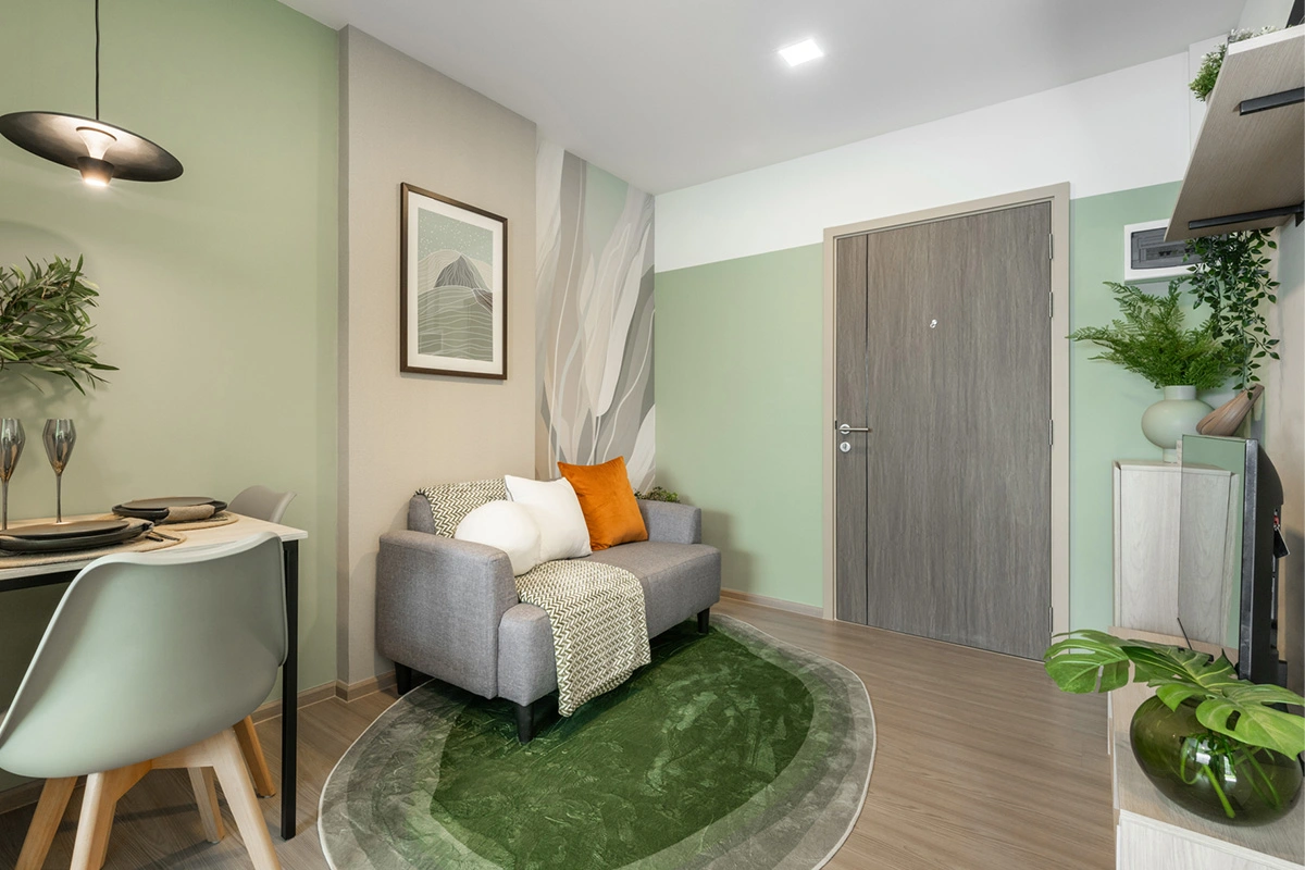 A living area in greens: a two-seat sofa on a round rug, the entrance door behind it and a table for two on the left