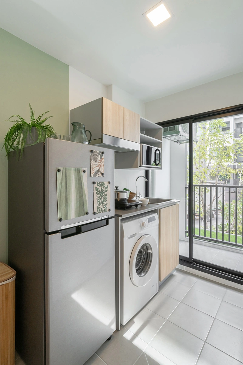 The kitchen niche: fridge, extractor hood and microwave over the sink, a washing machine under the counter and the balcony behind the sliding door