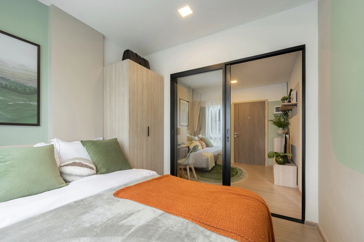 The bedroom from inside: the bed and wardrobe in front, with the living area and the entrance door seen through the clear sliding panel