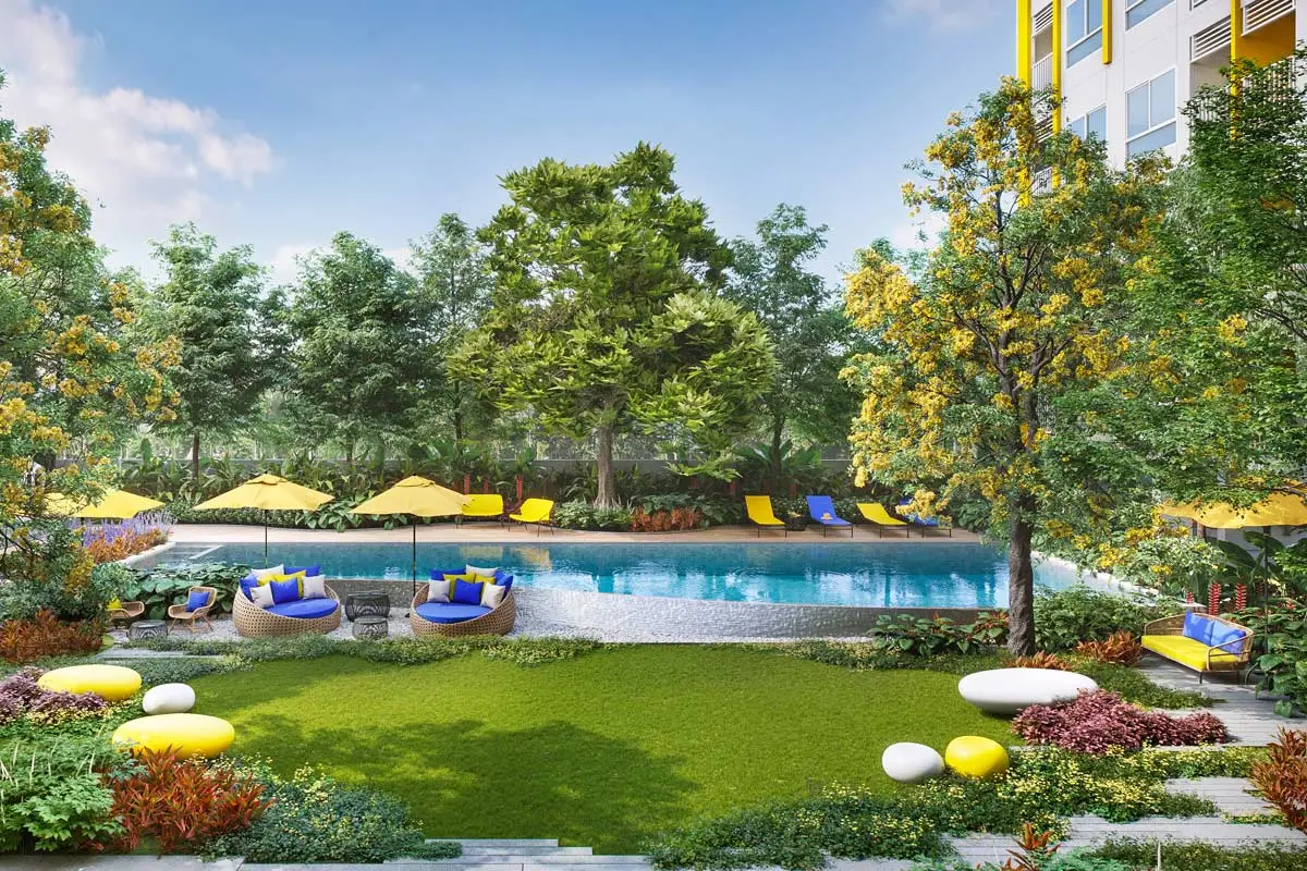 The courtyard from the lawn: yellow umbrellas and round wicker daybeds by the water, mown grass, shrubs and trees along the fence