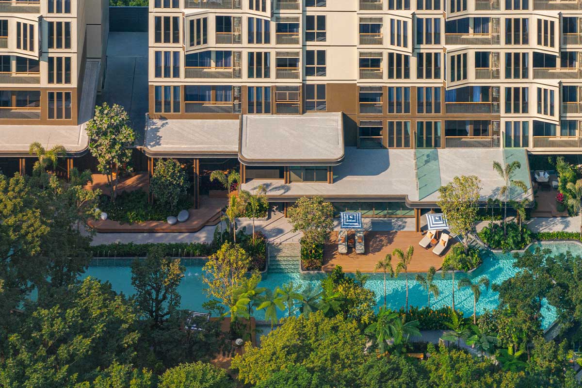 From above: the pool wraps in two arms around a timber deck with parasols and loungers, under the canopies of the communal area and facades of bay windows