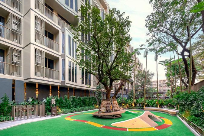 The dog run: artificial turf with coloured markings, a ramp and a tunnel, a round woven bench around a tree and a gate with a bone on it