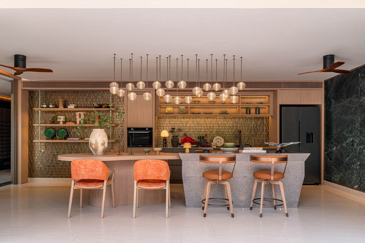 The Pantry Corner: a built-in oven and a tall tap against a gold-tiled wall, lit open shelving, a stone island with bar stools and globe pendant lights