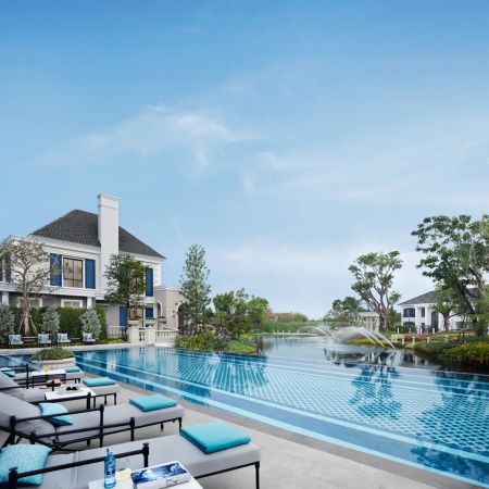 The pool alongside the water: loungers, a tiled deck and the buildings behind the trees