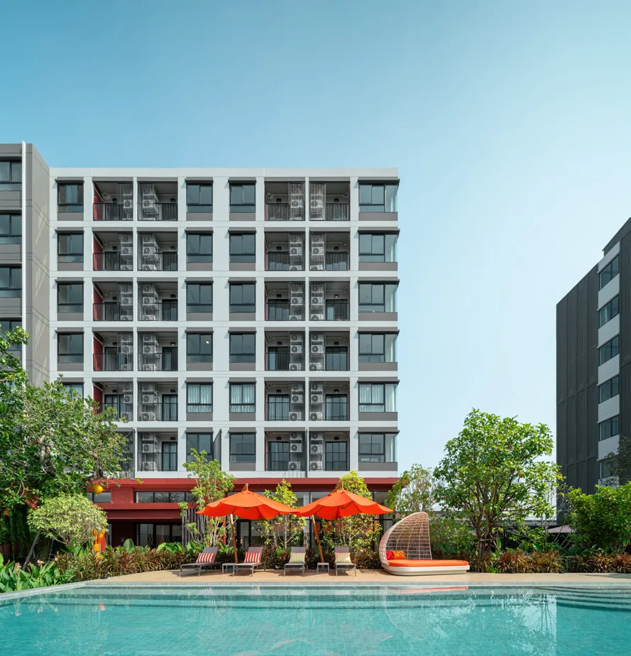 The building above the pool: red parasols and loungers at the water's edge
