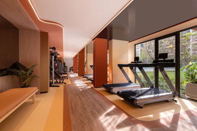 The gym along the glazing: treadmills, machines and greenery beyond the glass