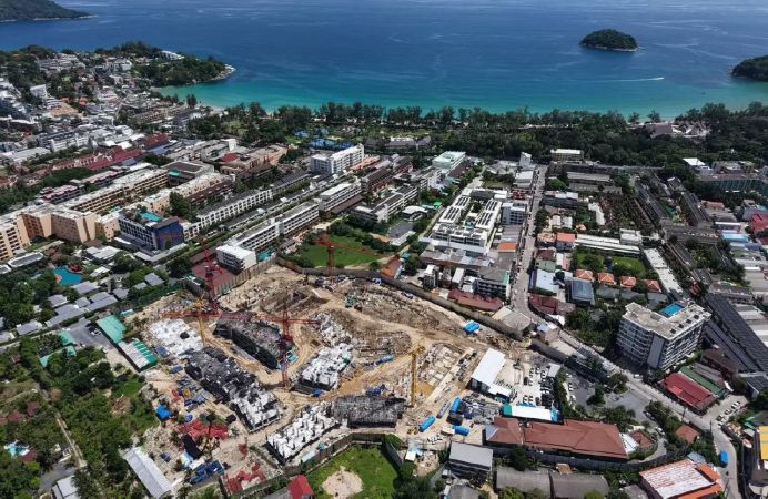 The site from the air in July 2026: excavation and cranes, Kata bay beyond the plot