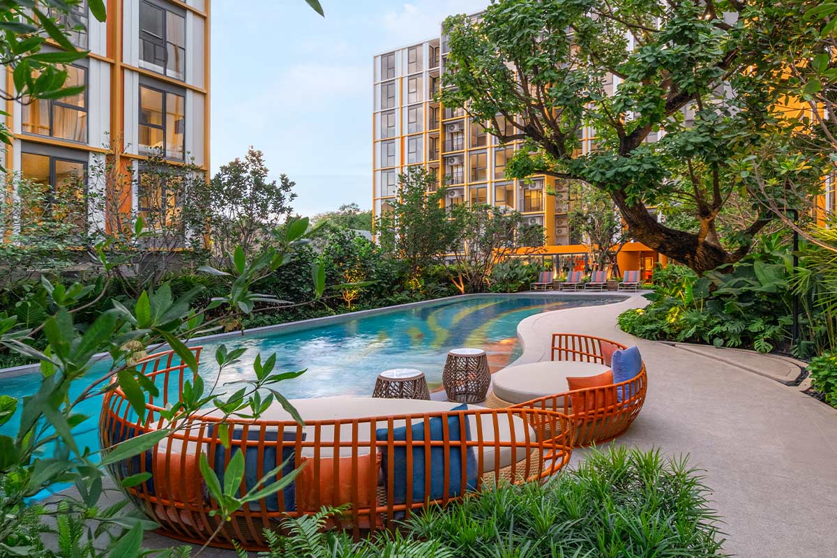 Round rattan daybeds by the water under the trees, with the buildings behind