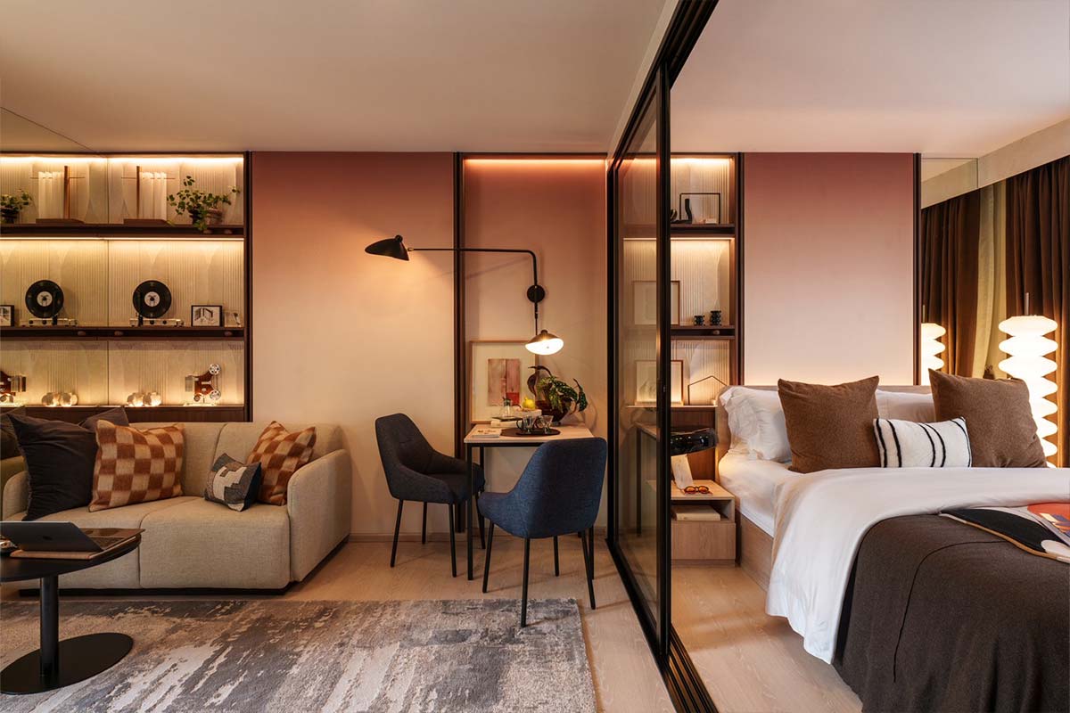 Show unit in terracotta tones: a sofa, a dining table for two and the bedroom behind a glass door