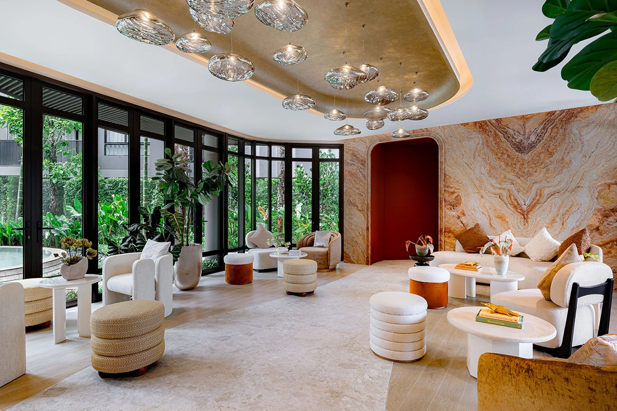 The lobby: full-height glazing, a wall of orange-and-white marble with a red arched niche, a cluster of glass pendants and round white armchairs