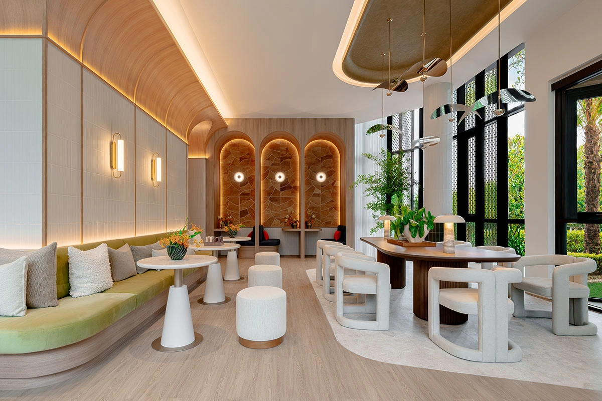 The co-working lounge: pale timber, lit arched niches, a long banquette along the wall, rounded white chairs and small round tables
