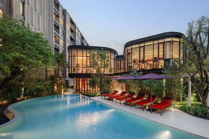 The pool at dusk: two glazed pavilions glowing from within and red loungers along the water
