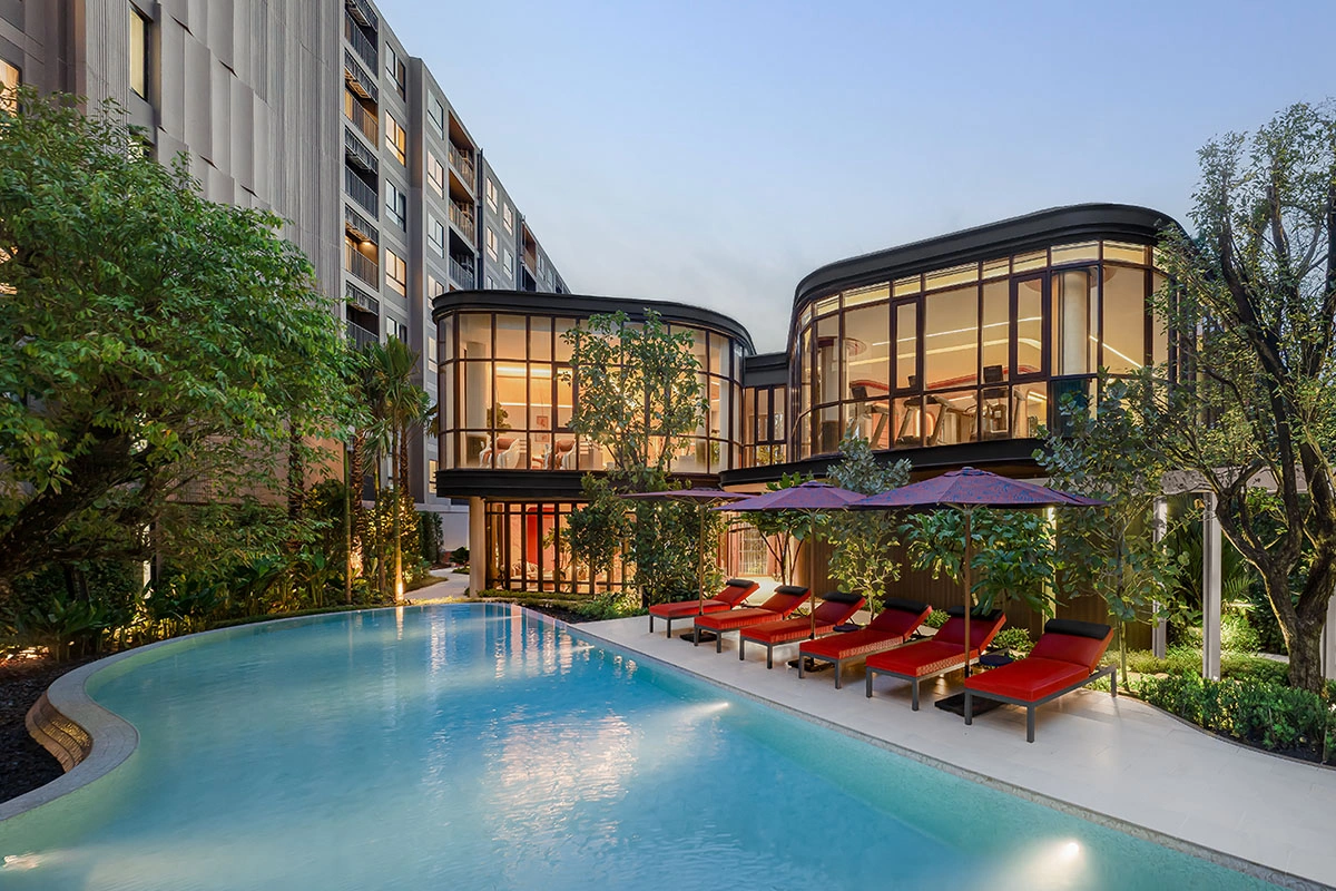 The pool at dusk: two glazed pavilions glowing from within and red loungers along the water