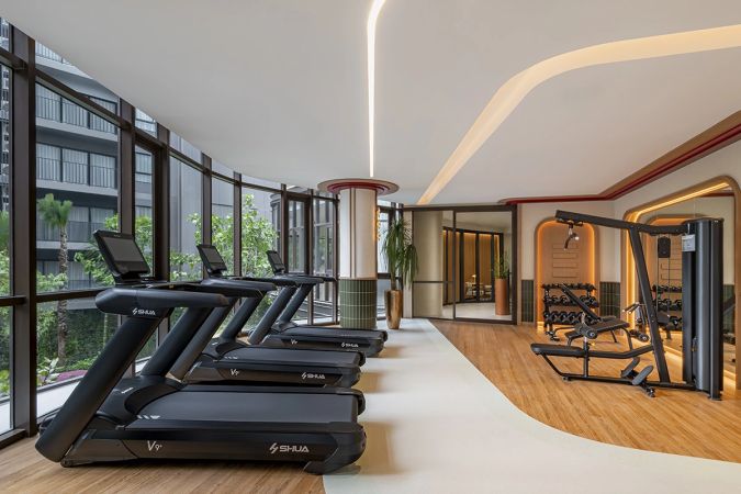 The fitness room: treadmills along the full glazing, a weights machine and a dumbbell rack further in, a timber floor and a wavy ceiling