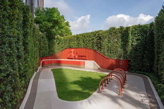 The Pet Park: a lawn framed by tall green hedge walls, a red wavy wall with a sign and red hoops for a dog agility course