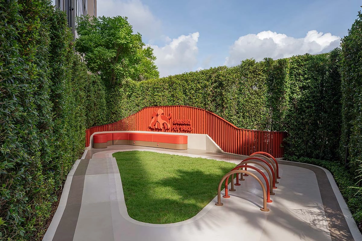 The Pet Park: a lawn framed by tall green hedge walls, a red wavy wall with a sign and red hoops for a dog agility course