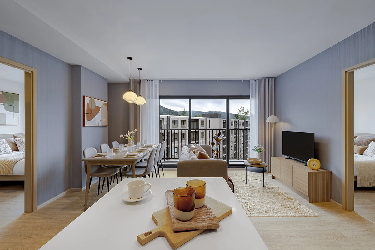 The living room of a two-bedroom unit seen from the kitchen: grey-blue walls, a dining table for six, a sofa, a TV cabinet and doors to both bedrooms on either side