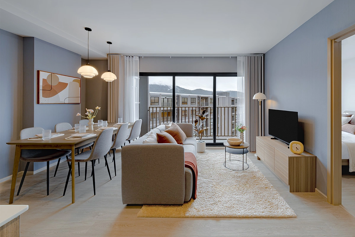 The same living room from the other side: the dining group, the sofa, the TV, a sliding door to the balcony and a view of the neighbouring wing and the hills