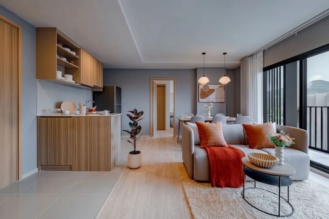 A one-bedroom unit: the timber kitchen with a counter on the left, a sofa with orange cushions and, beyond it, the dining group and the balcony