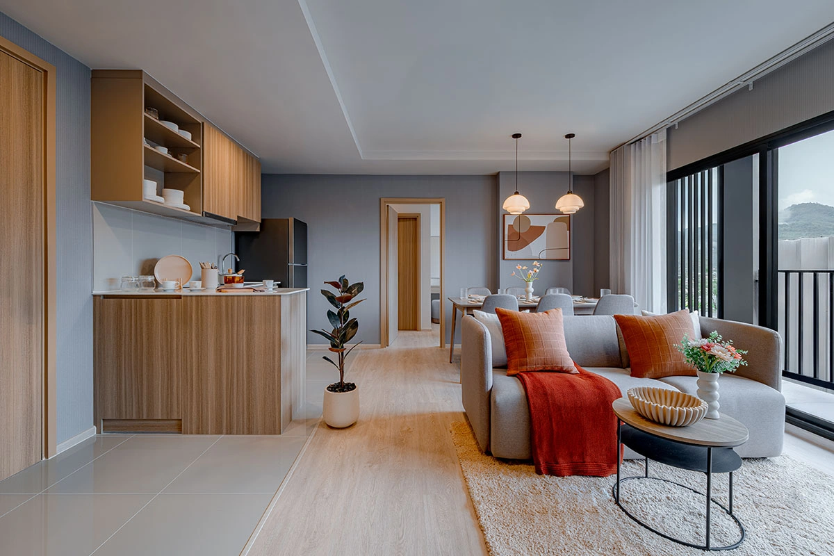 A one-bedroom unit: the timber kitchen with a counter on the left, a sofa with orange cushions and, beyond it, the dining group and the balcony