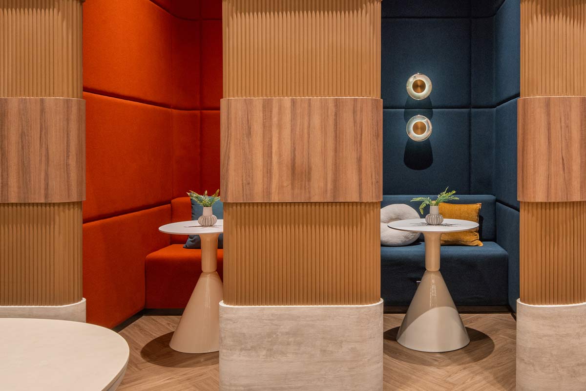 The private pods: fluted timber partitions, sofas upholstered in orange and dark blue, round tables on conical bases