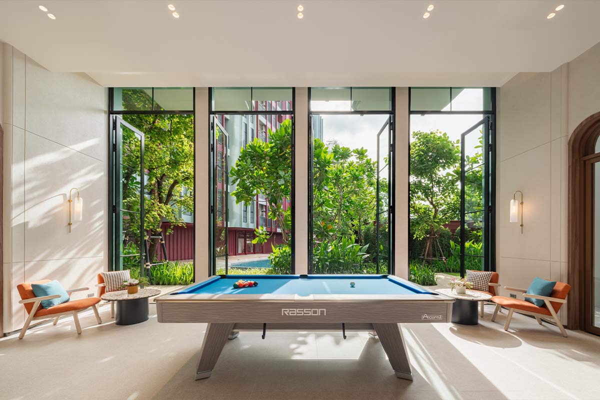 The entertainment room: a billiard table in the middle, folding glass doors opened onto the garden, armchairs and wall lamps