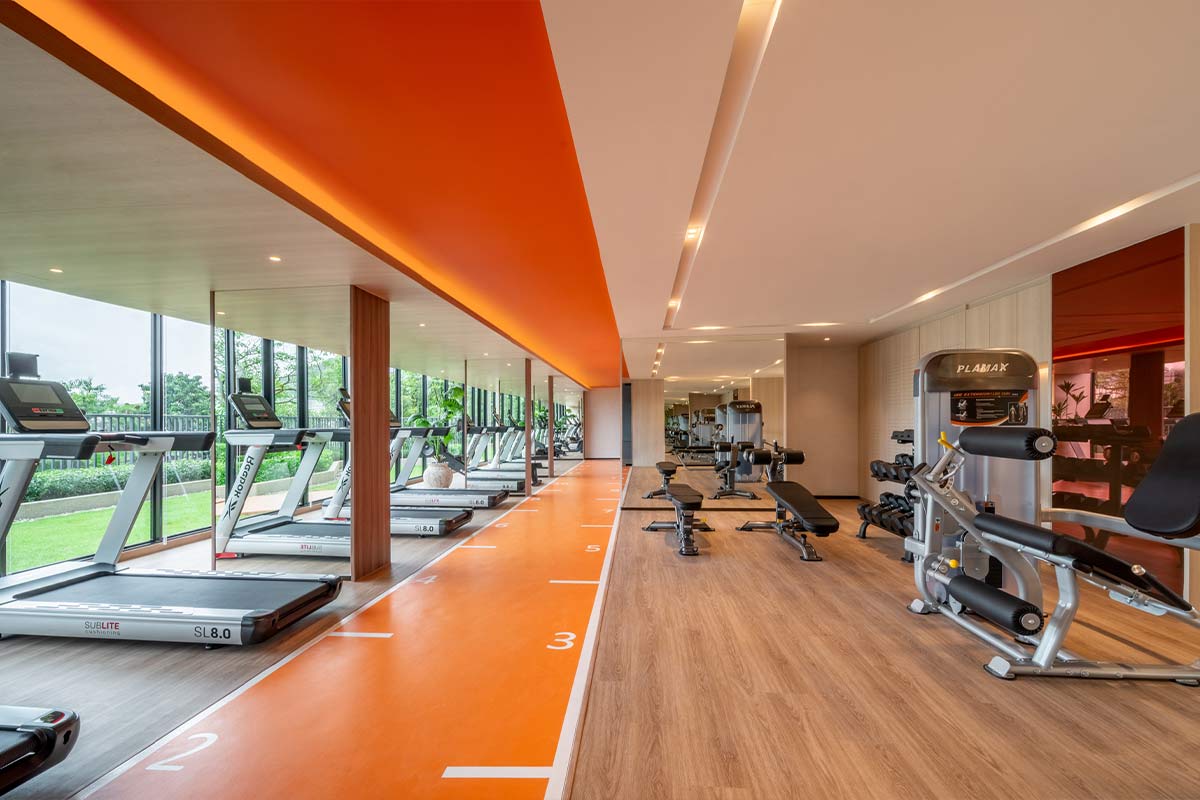 The fitness room: treadmills along the windows, an orange running strip with lane markings, benches with free weights and strength machines