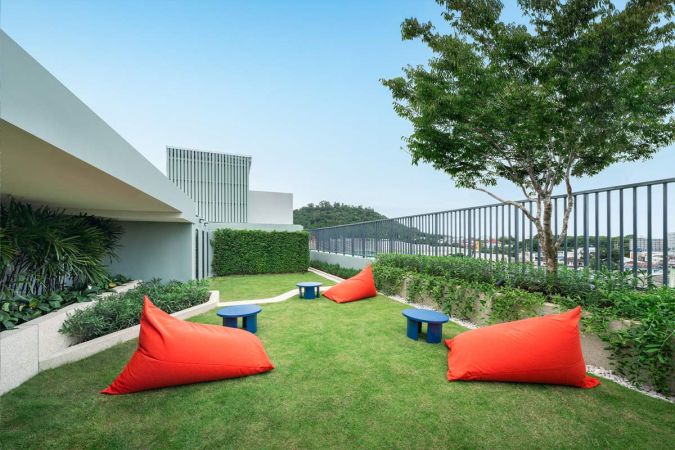 The rooftop garden: a mown lawn with red beanbags and low blue tables, a tree by the railing and the town beyond