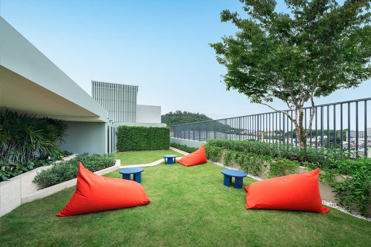 The rooftop garden: a mown lawn with red beanbags and low blue tables, a tree by the railing and the town beyond