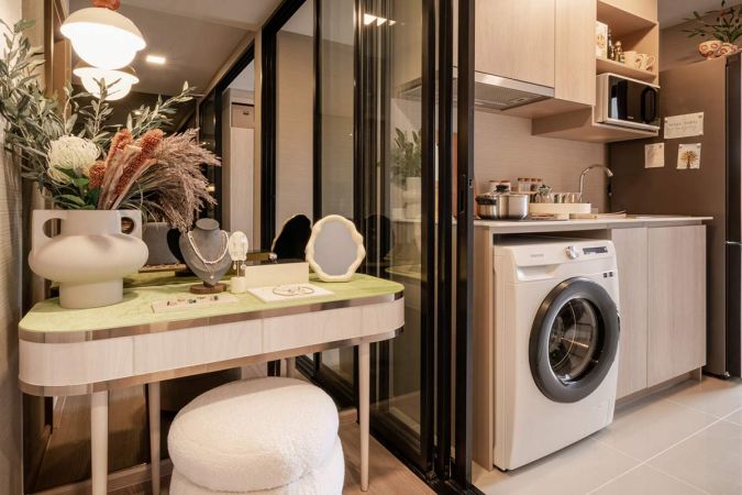 A dressing table with a light-green top by the glass partition, and behind it the kitchen with a washing machine under the counter and a microwave