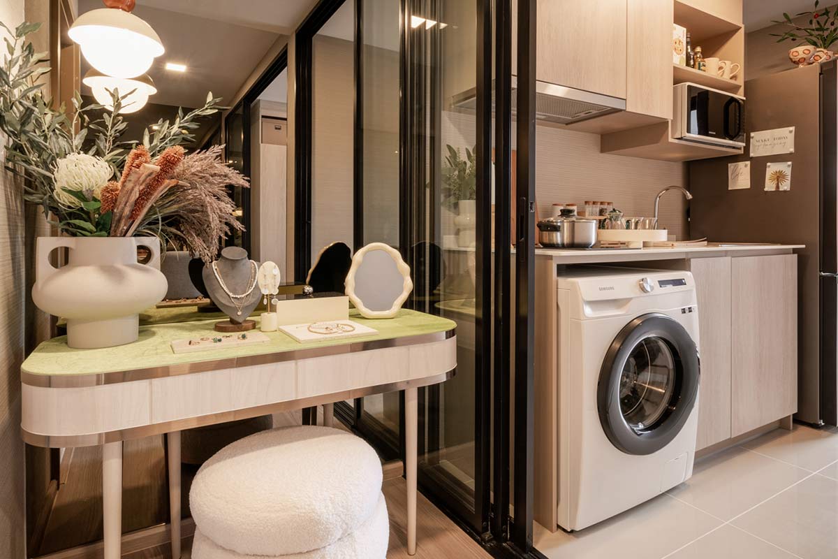 A dressing table with a light-green top by the glass partition, and behind it the kitchen with a washing machine under the counter and a microwave