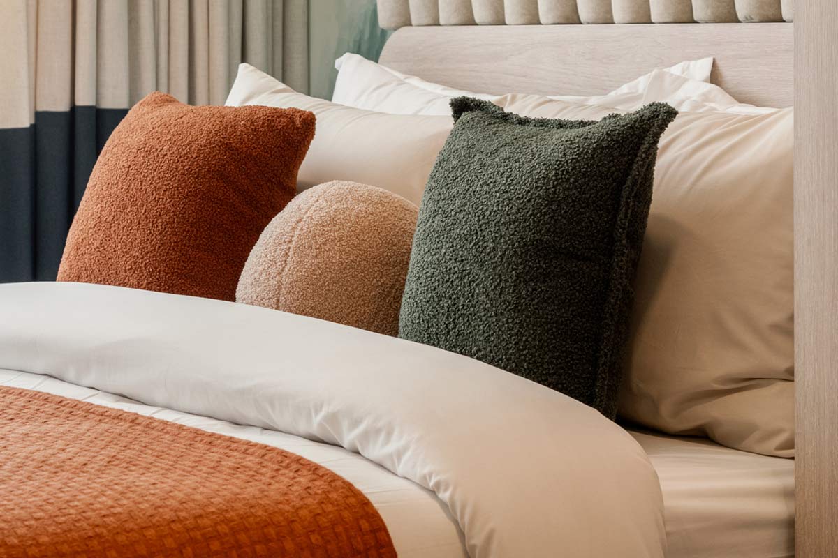 A close-up of the bed head: rust, beige and dark-green boucle cushions on white bedding