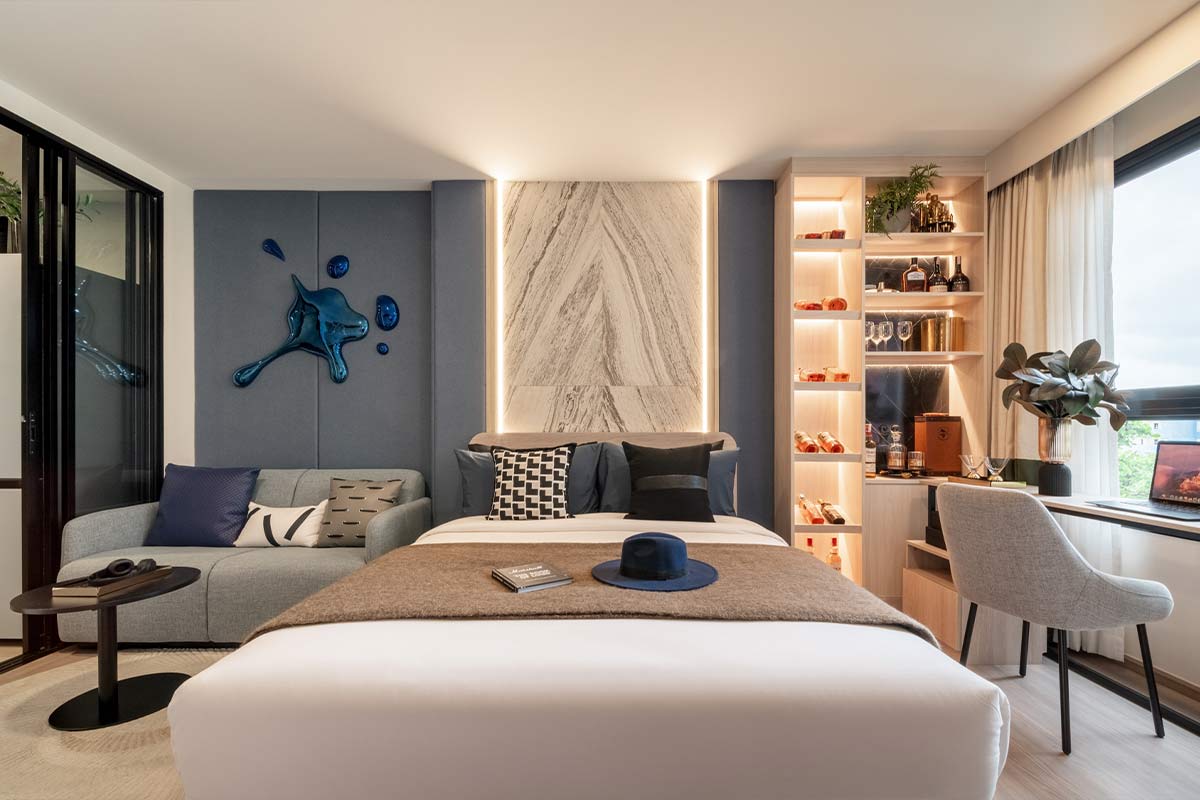 A larger show unit: the bed against a backlit marble panel, a grey sofa on the left, a lit shelving unit and a desk by the window